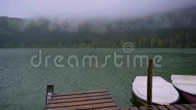 小船漂浮在靠近木墩的湖面上。 平静的山湖表面。 雾蒙蒙的山林