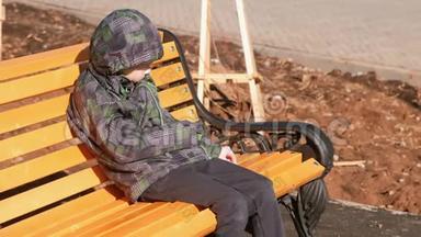 男孩坐在公园的长凳上，用石头划伤长凳。