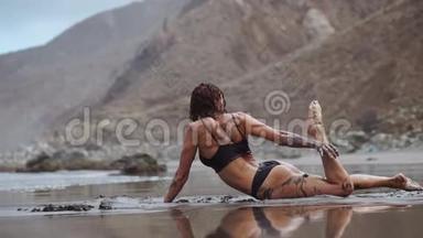美丽的女人穿着泳装在海滩上跳舞，沙滩上有黑色的沙子，靠近大海