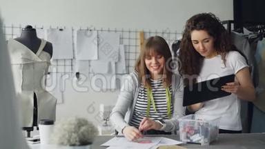 年轻的服装设计企业家正在观看平板电脑，并在草图上选择服装的面料颜色。 裁缝是