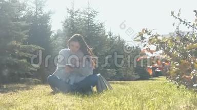 年轻美丽的黑发女子坐在草地上的<strong>春风</strong>公园，并键入一个信息在手机。