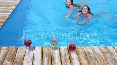 三位穿<strong>比基尼</strong>的年轻<strong>女士</strong>喝着五颜六色的鸡尾酒，在游泳池的蓝色水中放松