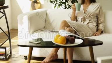 手里拿着杯子的女孩坐在沙发上喝着新鲜果汁