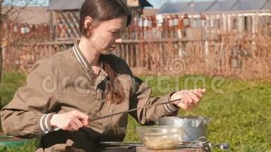 年轻的女人把肉放在扦子上。 做猪肉串。 她女儿四处<strong>走动</strong>。