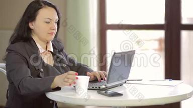 年轻的女人在咖啡馆的一张桌子上，在笔记本电脑后面工作，喝咖啡。 慢点。