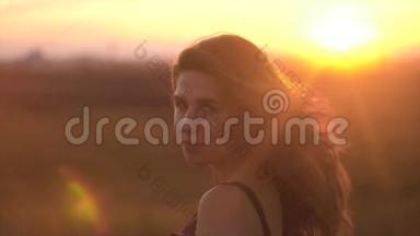 美丽的长发女人的肖像，背景是夕阳的阳光。 头发飘动的迷人女子