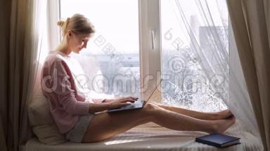 坐在窗台上用笔记本电脑工作的女人。 冬季<strong>天气晴朗</strong>