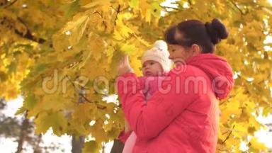 妈妈把婴儿抱在怀里，亲吻他的脸颊，向孩子展示黄色的叶子，然后笑。