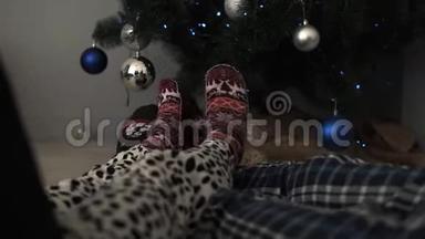 穿暖和冬袜的男女脚的细节，<strong>放在地板</strong>上，装饰精美的圣诞树和
