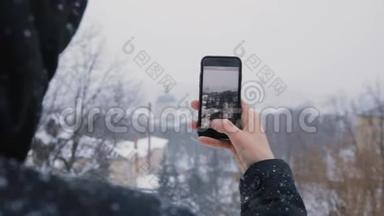 穿着黑色引擎盖的人使用电话显示了老城区和白雪皑皑的冬季公园的美景。 慢动作