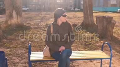 年轻漂亮的深褐色太阳镜的黑发女郎环顾四周，等着有人坐在多人的城市院子里的长凳上