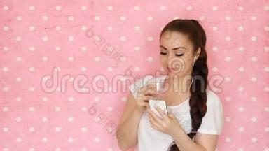 戴着耳机的年轻女人通过吸管喝水果奶昔，微笑着看着他的智能手机屏幕。 这就是