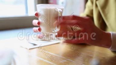 装有热泡牛奶的玻璃烧杯.. 女人在咖啡馆里把手放在一杯热牛奶上。 带着漂亮的拿铁