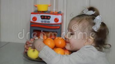 一个可爱的小女孩展示了她对水果的热爱。 孩子坐在一张桌子旁，吃橘子、橘子和苹果。
