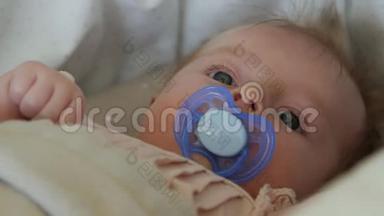 三个月的婴儿躺在毯子上用奶嘴。 宝宝`脸贴紧..