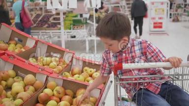 有趣的小男孩在超市的家庭购物中，坐在手推车里的盒子里摘<strong>苹果</strong>