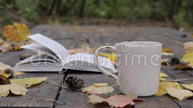 在旧木上有一本书，一杯茶-咖啡，落叶和锥。 风<strong>吹</strong>散<strong>树叶</strong>，移书页..