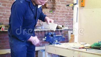 一个穿着工作服和安全眼镜的人把木制部分固定在老虎钳上。 木匠`车间。 工作过程