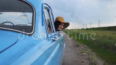 戴帽子的快乐女孩斜倚在复古车窗外，微笑着。 年轻快乐的女人望着老式老汽车的窗外
