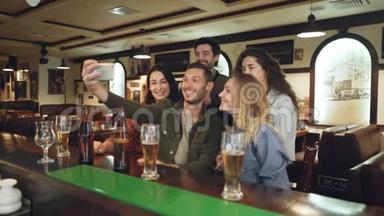 年轻人正在流行的酒吧里用智能手机自拍。 朋友们在摆姿势，玩得开心，打手势，笑。