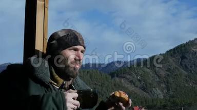 寂寞的胡须男站在观察甲板上看着一座山，喝着大杯子里的咖啡或茶。 慢慢慢慢