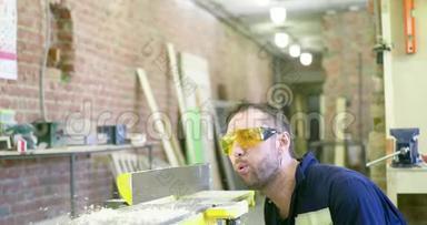 一个穿着工作服和安全眼镜的人把机器上的锯末吹掉。 木匠`车间。 工作