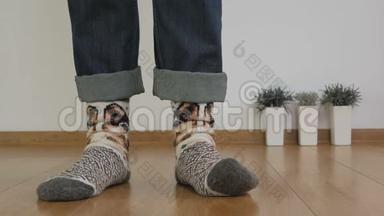 一个穿暖和羊毛袜的人的腿的特写站在房间的木地板上，踩着