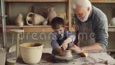 好奇的男孩正在小家庭工作室里向他有经验的祖父学习陶器。 小孩正在制作陶罐