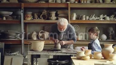 资深陶工正在纺抛轮成型粘土，而他的小孙子正在观看和学习。 分享