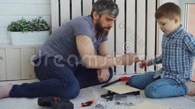 友好的父亲和小儿子在家里坐在地板上做建筑工程时谈笑风生