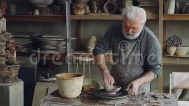 创意男陶器正在形成不对称的大碗在投掷轮，同时在小车间工作。 创造力