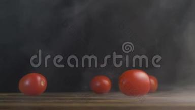 红色的小西红柿或樱桃西红柿卷在桌子上，在烟雾中缓慢地滚动