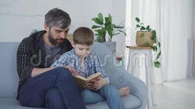可爱的父亲正在教他的孩子认真的学龄前<strong>儿童</strong>一边坐在沙发上<strong>看书</strong>。 绿色植物