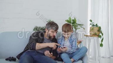 关爱的父亲正在教他好奇的小儿子使用智能手机。 男孩触摸屏幕，而胡子爸爸是