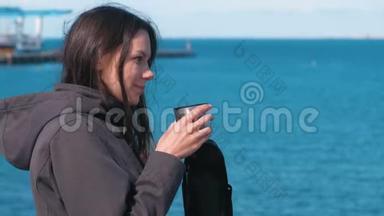女人在水边用热水瓶喝茶。 年轻的黑发女人在旅途中。