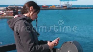 在阳光明媚的秋日，布吕内特女士在海边的海边，用手机输入一条信息。