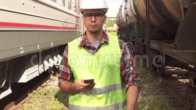 一个戴眼镜、戴头盔、穿制服的人拿着电话走在火车站的画像