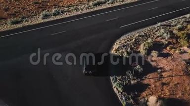 无人机跟随着银色的小型货车沿着不可思议的美国沙漠公路行驶，公路上有美丽的岩石山。