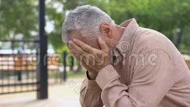 悲伤的老人坐在医院的花园长凳上，老人悲伤地哭泣