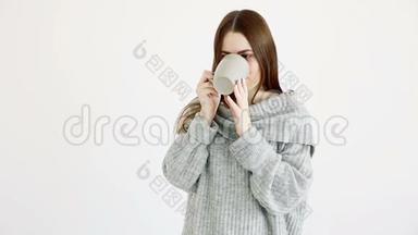 美丽的欧洲女孩穿着温暖的毛衣喝着<strong>白墙</strong>旁的热茶。