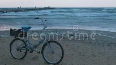 夕阳西下沙滩上的旧自行车，带着风暴的<strong>大海</strong>和泡沫的波浪<strong>背景</strong>，码头上有步行的人。