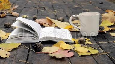 在旧木上有一本书，一杯茶-咖啡，落叶和锥。 风<strong>吹</strong>散<strong>树叶</strong>，移书页..