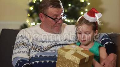 一个戴着圣诞帽的女孩抱着她的祖父，<strong>感谢</strong>他的<strong>礼物</strong>。 家庭平安夜