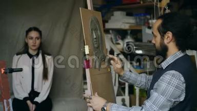 雕塑家在画室里给`摆姿势的年轻女子在画布上创作人的面部雕塑