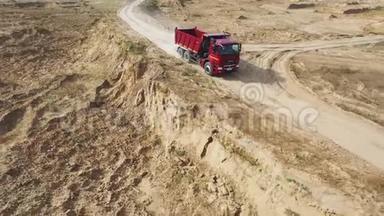 在狭窄的砂石跑道上移动的大型和空的红色自卸卡车。 场景。 从上面看