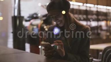 年轻漂亮、时髦的黑发女人晚上坐在靠近窗户的咖啡屋里，用电话