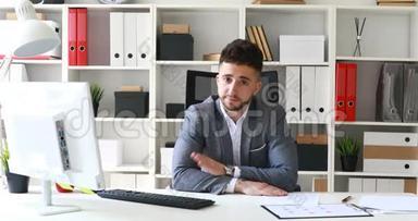 穿着灰色夹克的商人坐在白色办公室的桌子上，消极地摇头