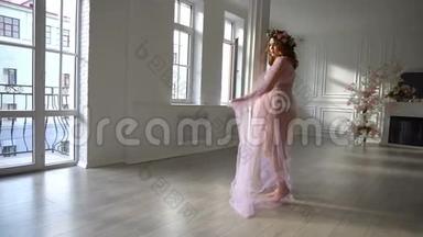年轻的孕妇穿着<strong>淡蓝色</strong>的粉红色裙子在家跳舞