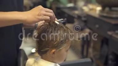 理发师在理发店给小男孩理发前梳头。 儿童用梳子理发