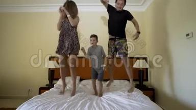幸福的一家人在床上跳。 幸福的家庭观念。 爸爸，妈妈和小男孩跳在床上